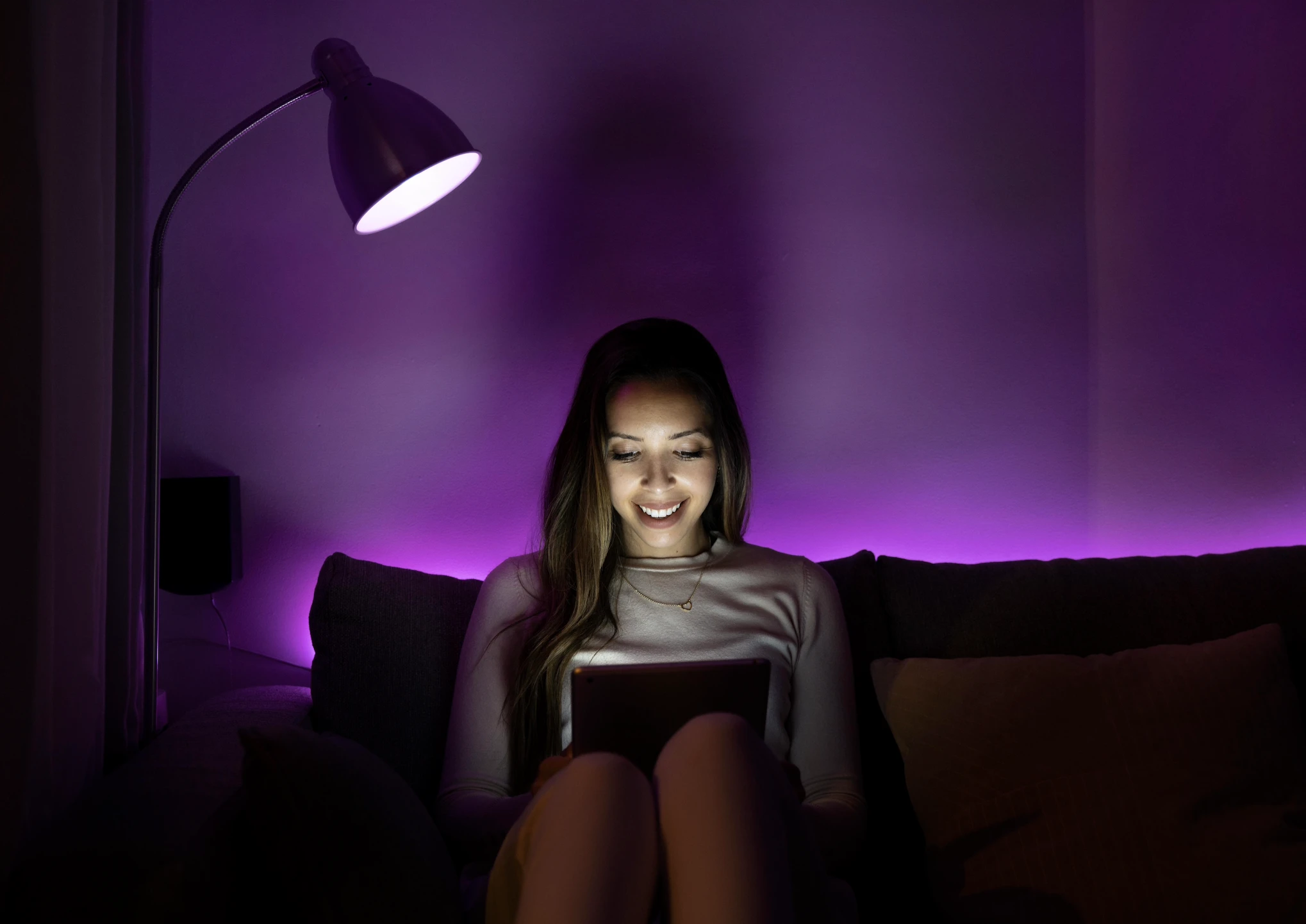 LED világításnál éjjel olvasó nő a kanapén.